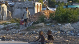 A Haitian man (L) carries a bucket filled with waste to be discarded, in a slum area in Port-au-Prince, Haiti, Dec. 17, 2012.